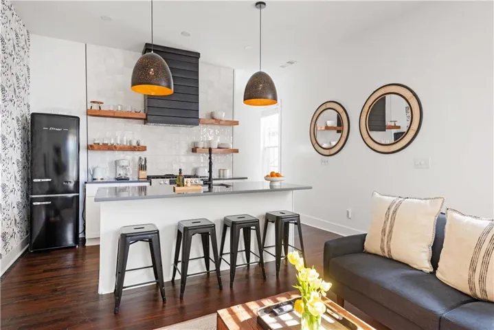 Kitchen with a breakfast bar area, decorative light fixtures, open shelves, tasteful backsplash, and dark wood-style flooring