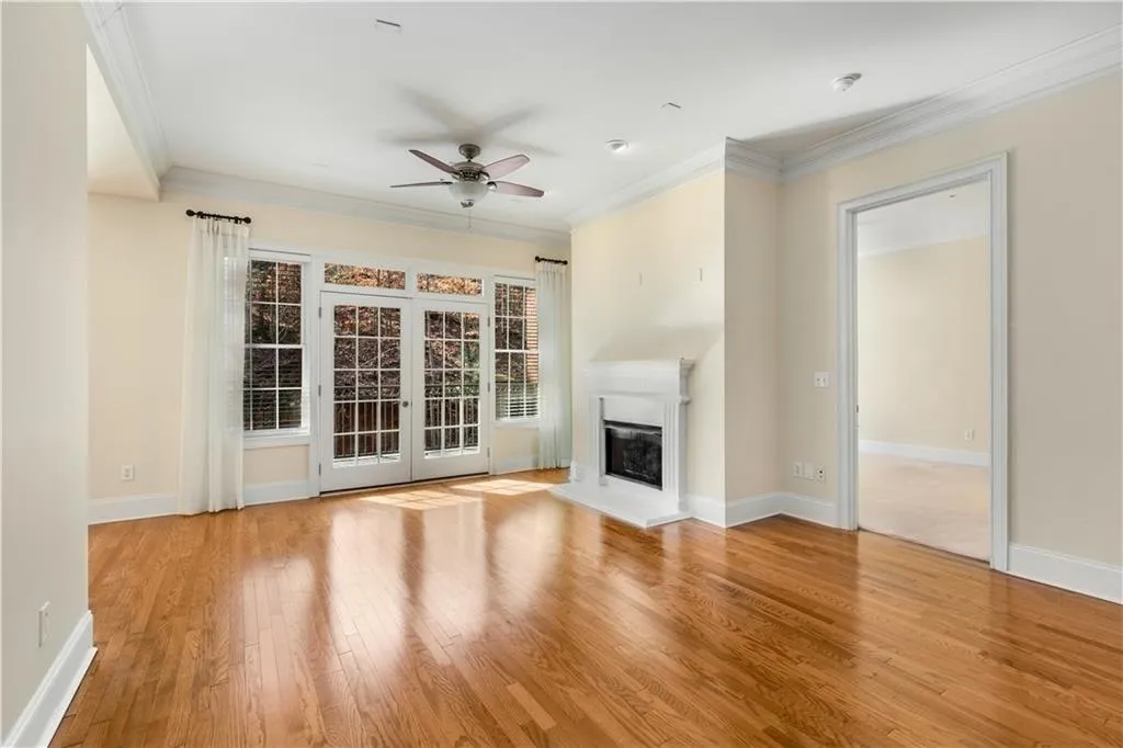 Present view of the Living Room with a view into the Primary Bedroom.  Note the beautiful floors and moldings, 10 feet ceilings, gas logs fireplace, ceiling fan with light and wall of glass with French doors for lots of natural light.