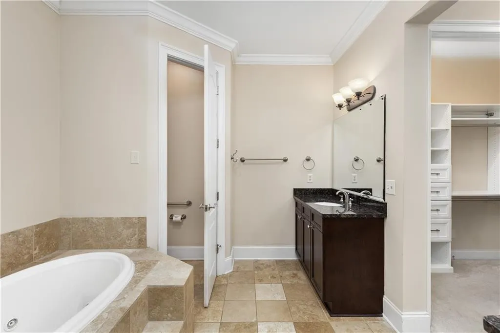 View of one of the vanities with the doors to the water closet and one of the walk-in closet open.