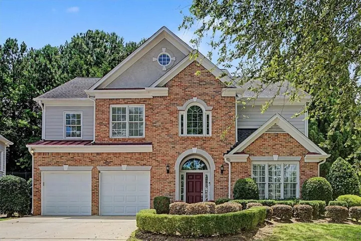 Brick and siding exterior featuring a prominent arched entry with a red door, a two-car garage, and mature front landscaping