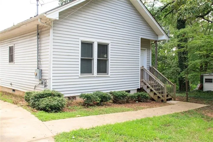Vinyl siding exterior with a side entry porch, wood steps, and mature perimeter trees