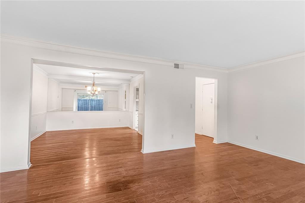 Unfurnished living room featuring crown molding, a chandelier, and hardwood / wood-style flooring Unfurnished living room featuring crown molding, a chandelier, and hardwood / wood-style flooring