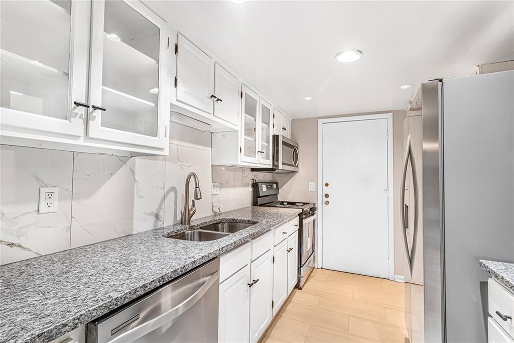 Kitchen featuring tasteful backsplash, white cabinetry, light stone counters, appliances with stainless steel finishes, and sink Kitchen featuring tasteful backsplash, white cabinetry, light stone counters, appliances with stainless steel finishes, and sink
