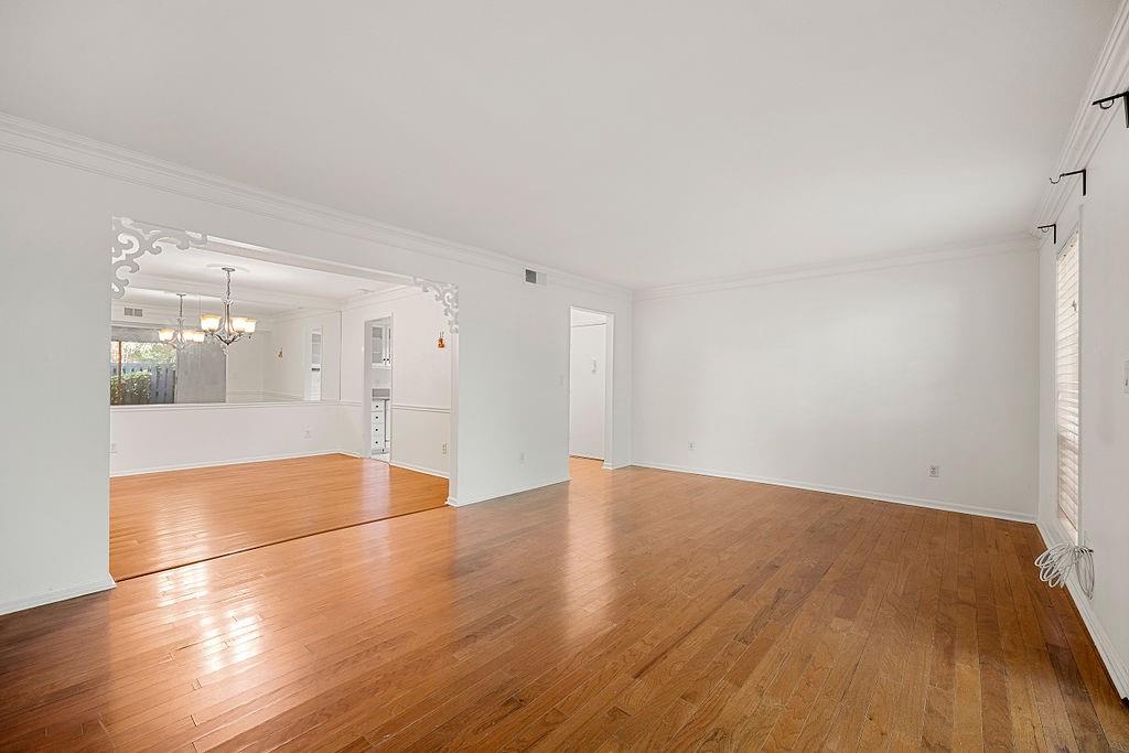Unfurnished room with ornamental molding, a notable chandelier, and light hardwood / wood-style flooring Unfurnished room with ornamental molding, a notable chandelier, and light hardwood / wood-style flooring