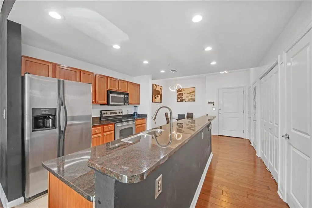 Kitchen with appliances with stainless steel finishes, sink, dark stone counters, light hardwood / wood-style floors, and a center island with sink