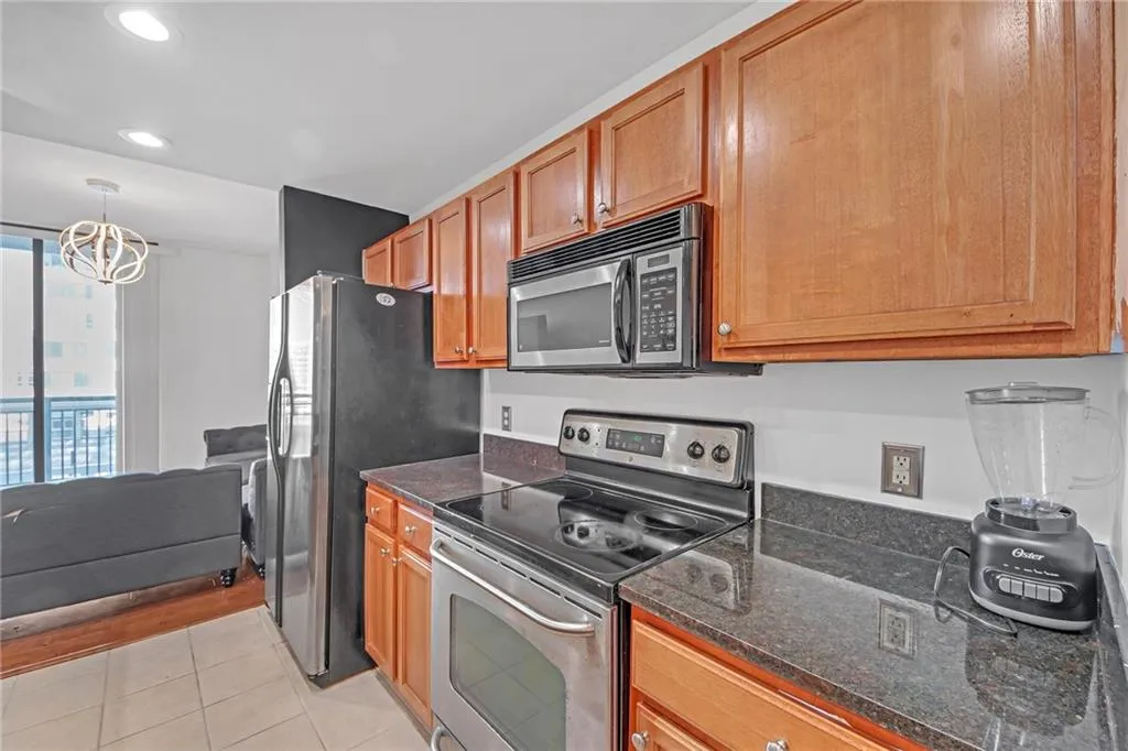 Kitchen featuring appliances with stainless steel finishes, dark stone counters, hanging light fixtures, light tile patterned floors, and an inviting chandelier