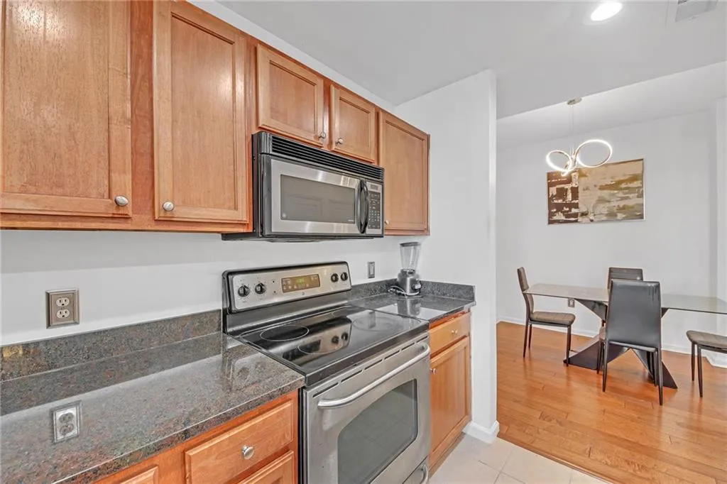Kitchen with stainless steel appliances, hanging light fixtures, light hardwood / wood-style flooring, and dark stone counters