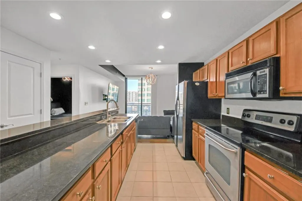 Kitchen with dark stone countertops, sink, light tile patterned flooring, and stainless steel electric range oven