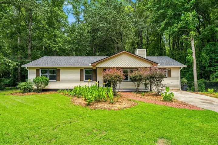 Ranch-style exterior with light-colored siding, dark shingle roof, and brown window shutters
