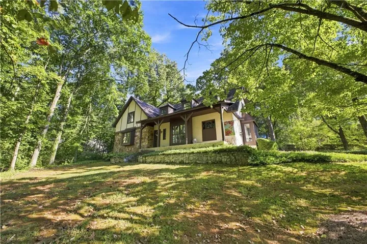 Tudor-style exterior with stone and stucco finishes, a dark shingle roof, and exposed timber detailing