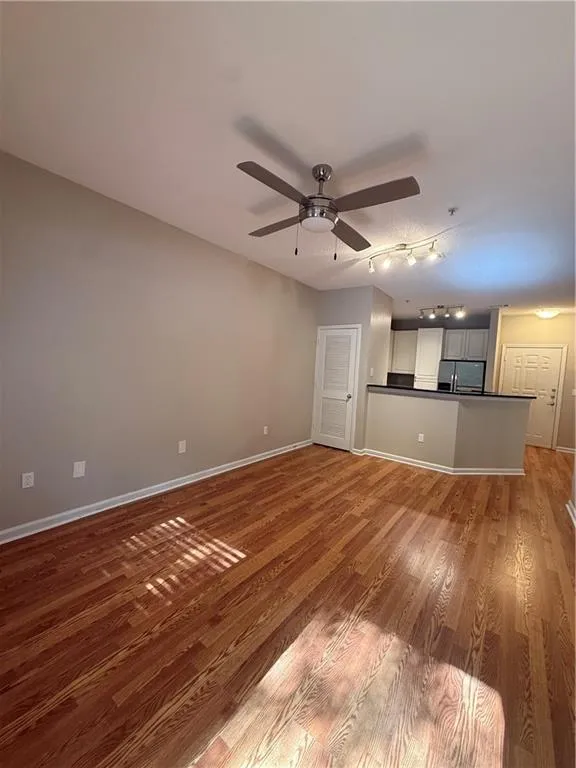 Unfurnished living room with track lighting, ceiling fan, and wood finished floors