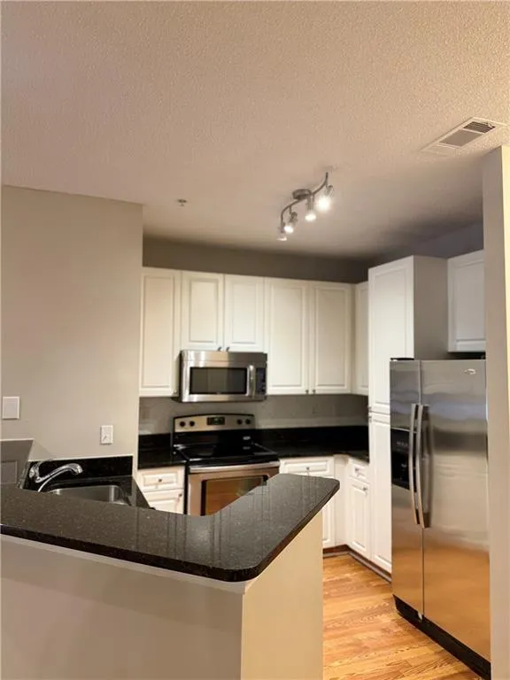 Kitchen featuring appliances with stainless steel finishes, a peninsula, white cabinetry, light wood-style floors, and dark stone counters