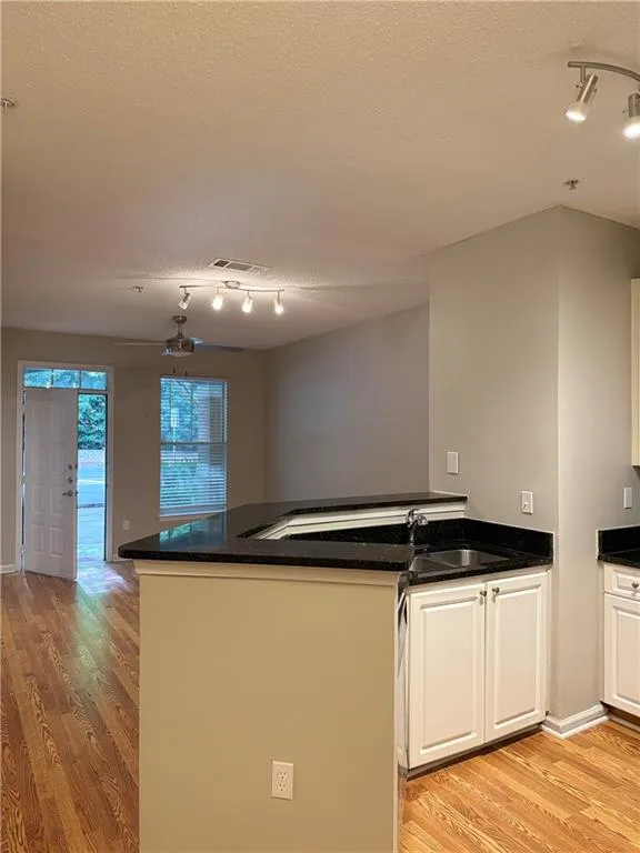 Kitchen with rail lighting, light wood-type flooring, white cabinets, a textured ceiling, and a peninsula