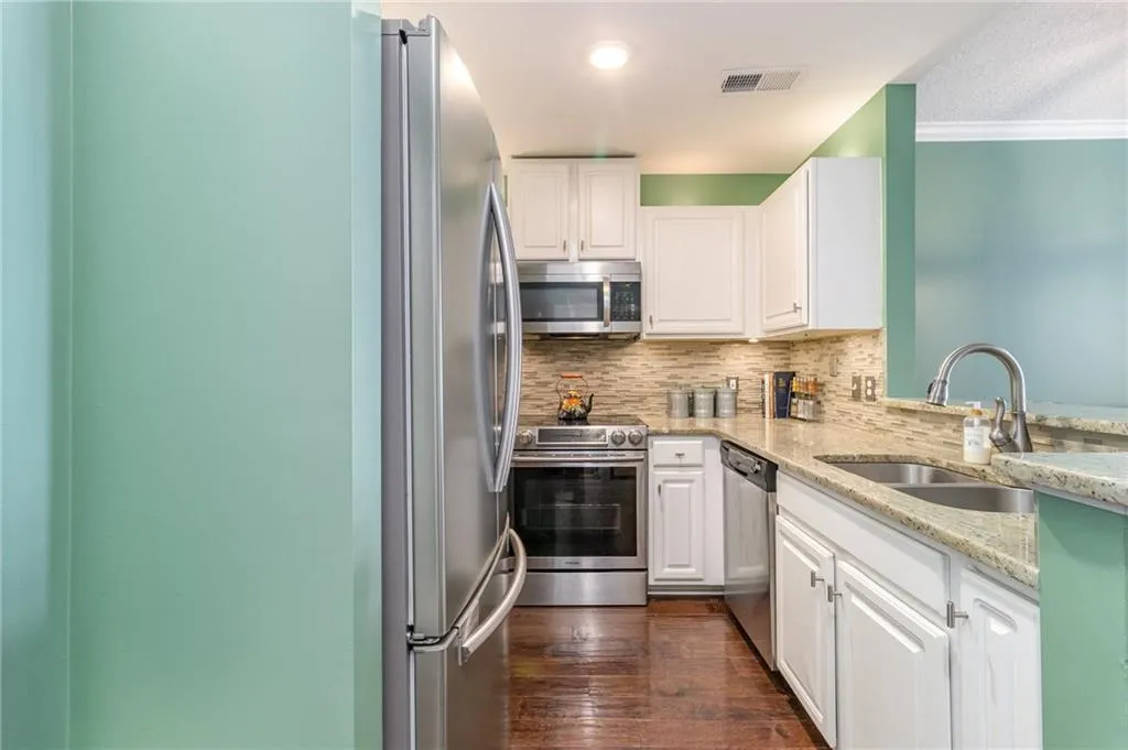 Kitchen with light stone countertops, appliances with stainless steel finishes, decorative backsplash, white cabinetry, and ornamental molding