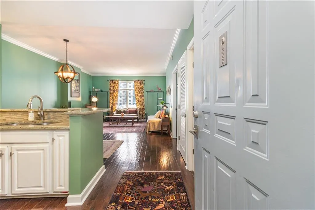 Kitchen featuring light stone counters, white cabinets, dark wood-style flooring, ornamental molding, and a chandelier