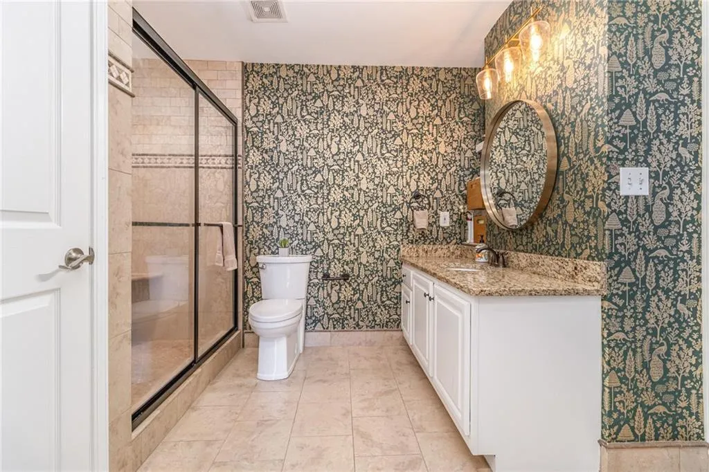 Bathroom featuring vanity, wallpapered walls, a shower stall, and light tile patterned floors