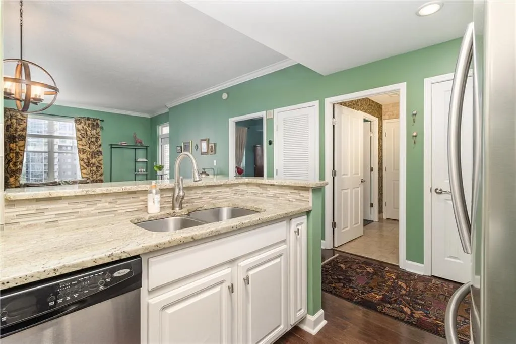 Kitchen with stainless steel appliances, white cabinets, light stone counters, dark wood-style floors, and ornamental molding