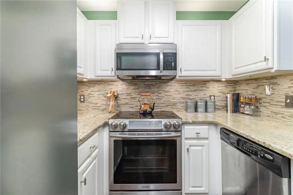Kitchen featuring appliances with stainless steel finishes, white cabinetry, light stone counters, and decorative backsplash