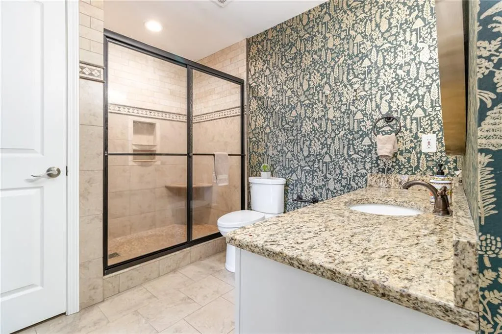 Full bath featuring vanity, wallpapered walls, a stall shower, and light tile patterned floors