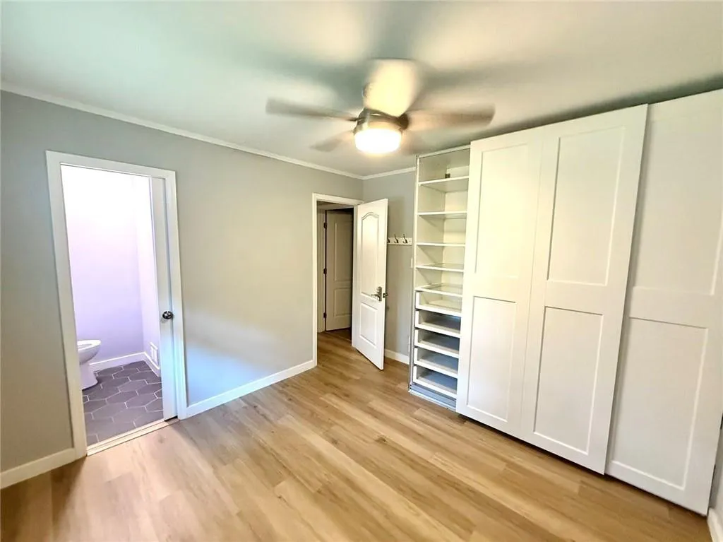 Unfurnished bedroom with light wood-style flooring, crown molding, connected bathroom, and a ceiling fan