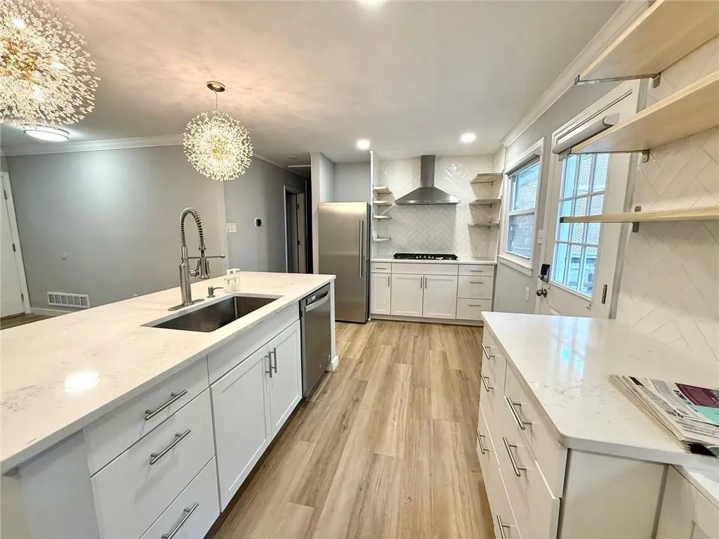 Kitchen with open shelves, wall chimney range hood, appliances with stainless steel finishes, decorative backsplash, and ornamental molding