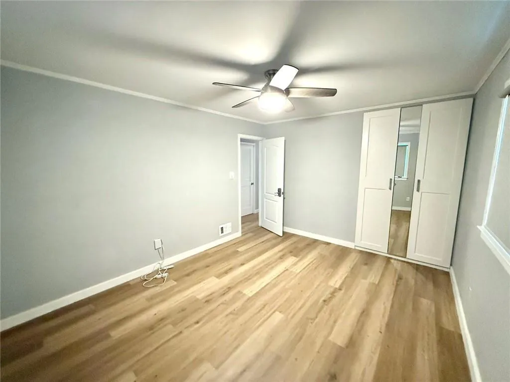 Unfurnished bedroom featuring light wood finished floors, ornamental molding, and a ceiling fan