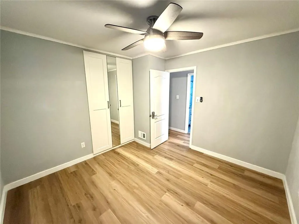 Unfurnished bedroom featuring light wood-style flooring, crown molding, a closet, and a ceiling fan