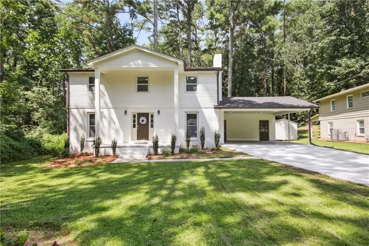 Two-story residence with a covered front porch, an attached carport, a paved driveway, and a white brick and siding exterior