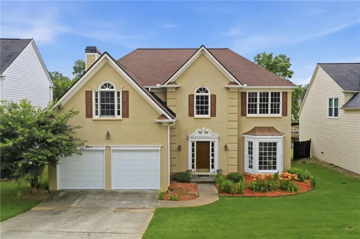 Stucco facade residence featuring a two-car garage, prominent bay window, arched window details, and a landscaped front yard with a paved walkway