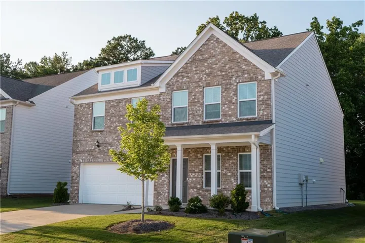 Two-story residence featuring a brick and siding exterior, front porch with columns, attached garage, and dormer window