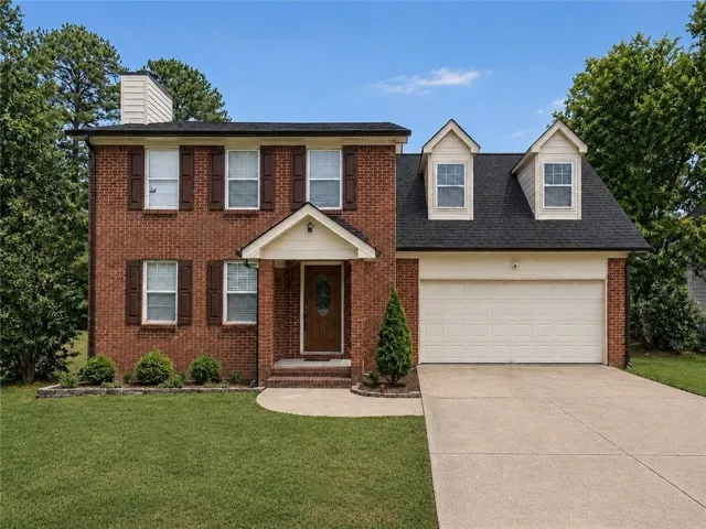 Brick exterior with dormer windows, a covered entry, an attached two-car garage, and a concrete driveway