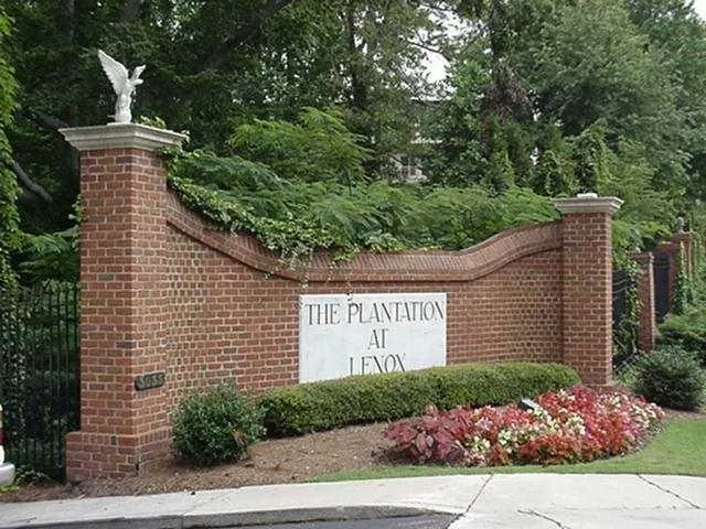 Brick entry monument with an ornate pillar topper, integrated signage, wrought iron fencing, and vibrant landscaping