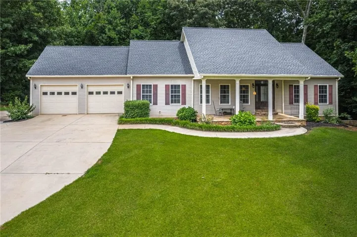 Ranch-style residence featuring a two-car garage, covered front porch, and mature landscaping