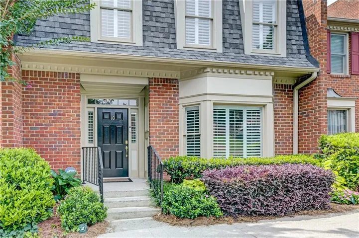 Brick facade featuring a black paneled front door with sidelights, a slate-style mansard roof, and a bay window with white plantation shutters