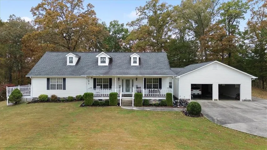 Cape cod house featuring a porch, an attached garage, a front lawn, a shingled roof, and concrete driveway