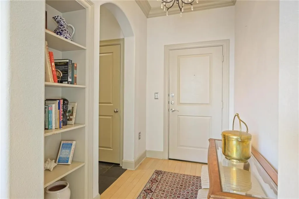Doorway to outside featuring wood finished floors, crown molding, arched walkways, a chandelier, and built in features