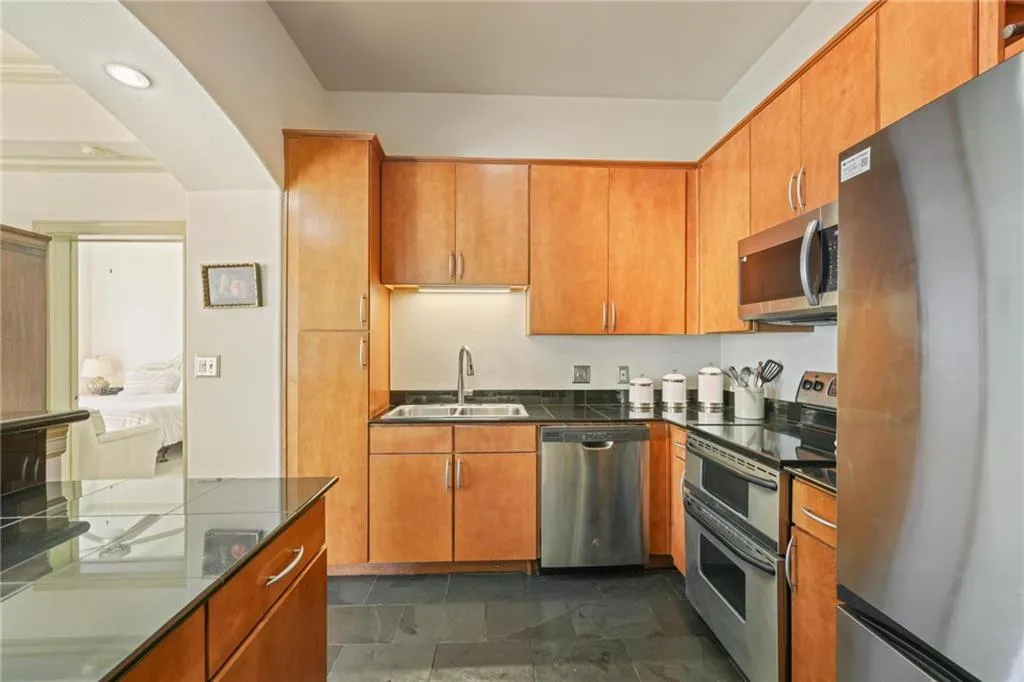 Kitchen with appliances with stainless steel finishes, arched walkways, stone tile flooring, brown cabinets, and recessed lighting