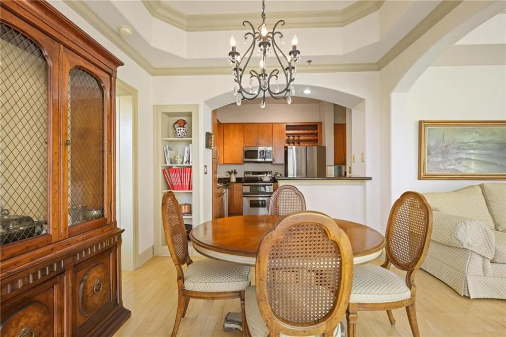 Dining room with light wood-style floors, ornamental molding, a raised ceiling, arched walkways, and a chandelier