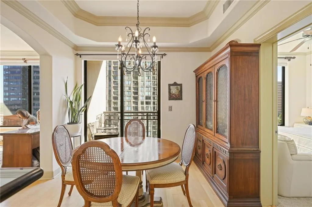 Dining room featuring crown molding, wood finished floors, a tray ceiling, arched walkways, and a chandelier