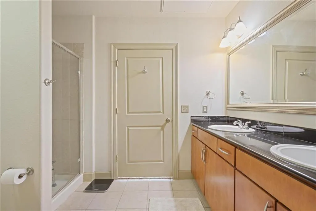 Full bathroom featuring light tile patterned floors, a shower stall, and double vanity