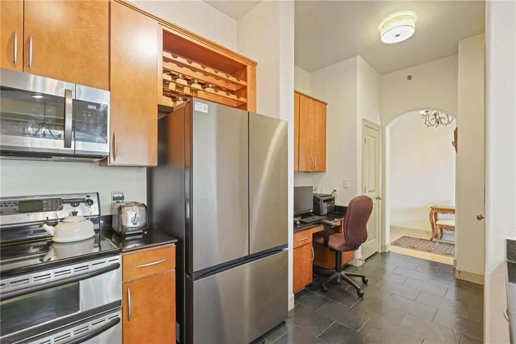 Kitchen featuring appliances with stainless steel finishes, brown cabinets, dark tile patterned floors, arched walkways, and built in desk