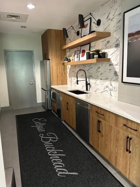 Kitchen featuring dishwasher, fridge, light countertops, open shelves, and brown cabinets
