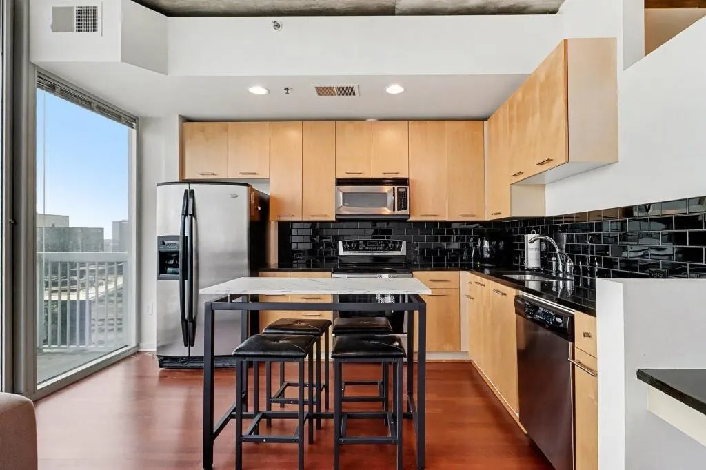 Contemporary Kitchen Features Light Maple Cabinetry, Stainless Steel Appliances, & Black Subway Tile