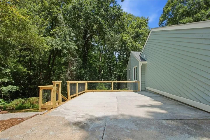 Expansive concrete patio with a new wood deck featuring black metal balusters