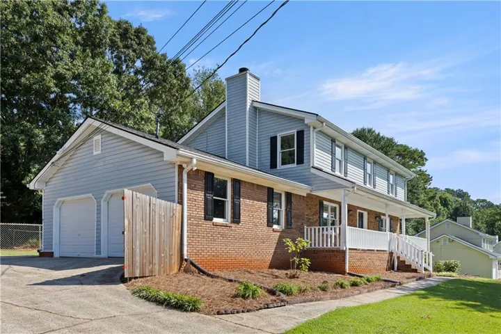 Traditional architecture featuring a brick and siding exterior, a multi-story design, an attached two-car garage, an elongated covered front porch, and a dormer window