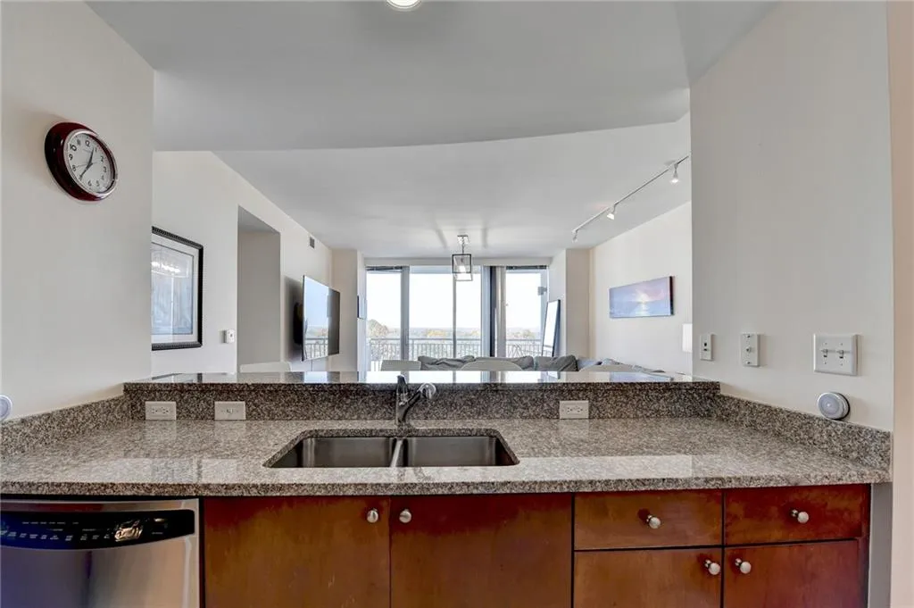 Kitchen with sink, rail lighting, stainless steel dishwasher, light stone counters, and kitchen peninsula