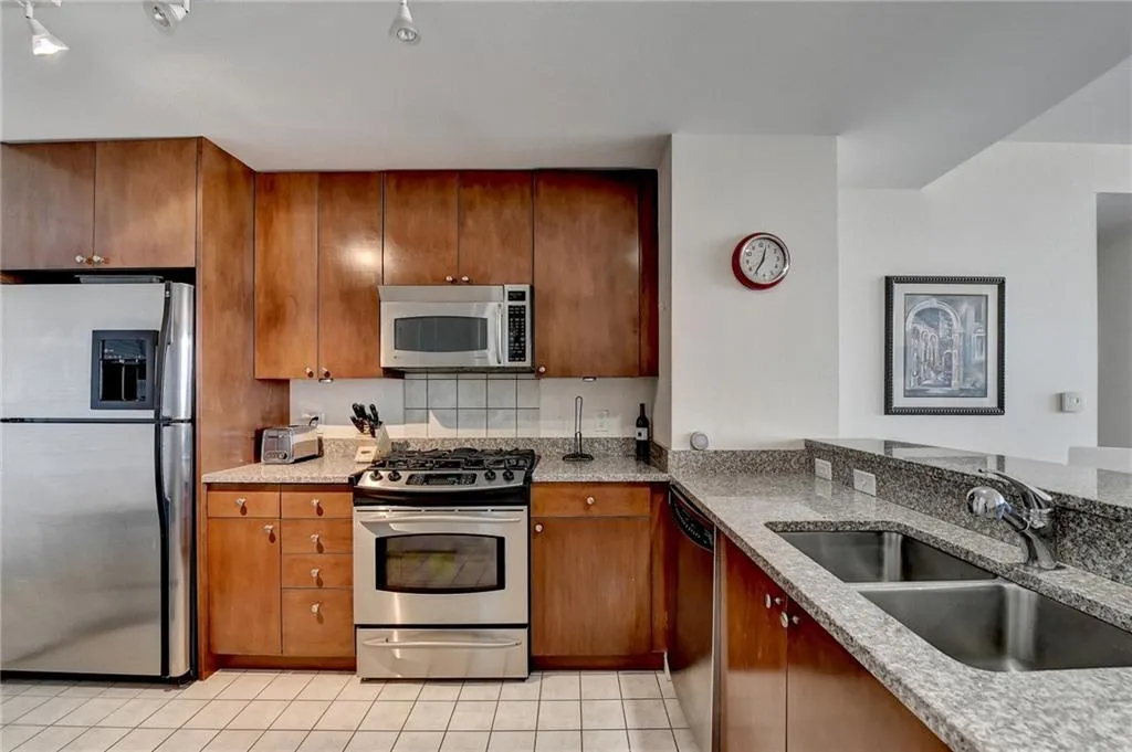 Kitchen featuring light tile patterned floors, stainless steel appliances, light stone counters, and sink