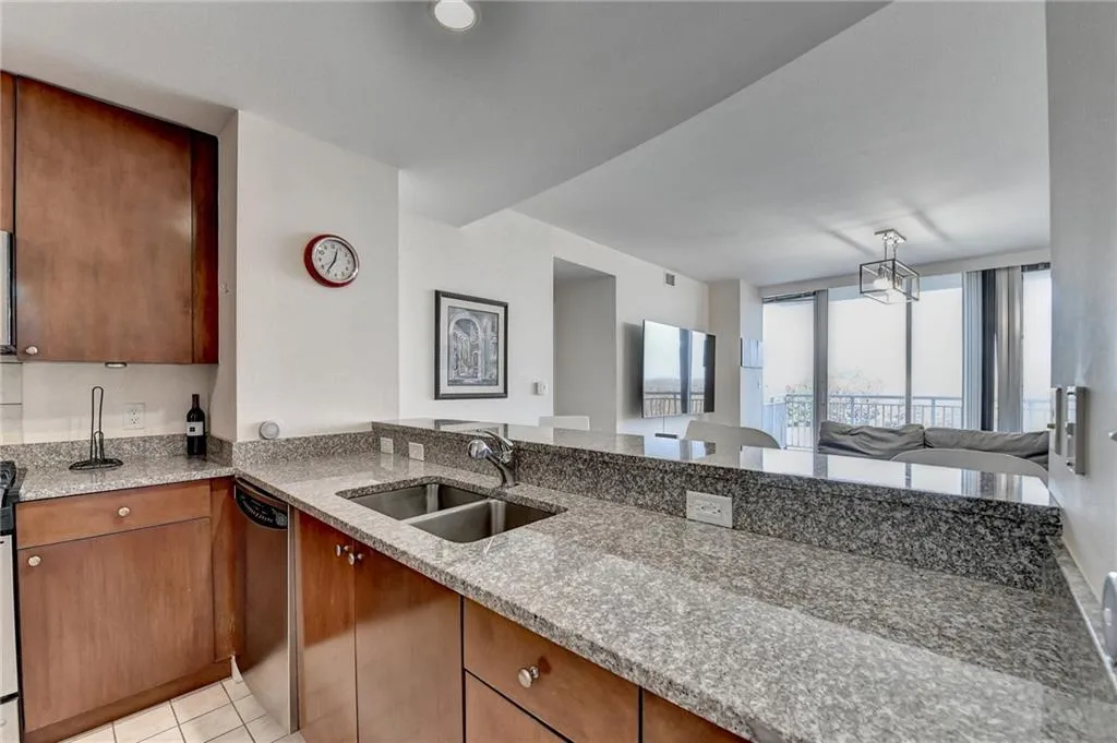 Kitchen featuring sink, stainless steel dishwasher, light tile patterned floors, light stone counters, and kitchen peninsula