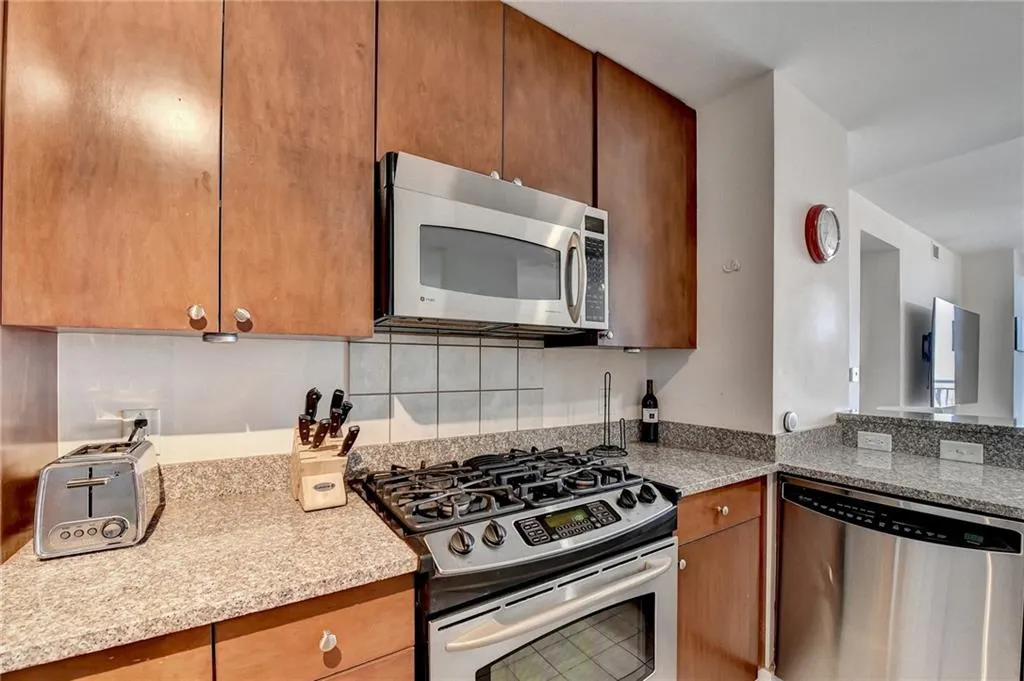 Kitchen with light stone countertops, backsplash, and stainless steel appliances