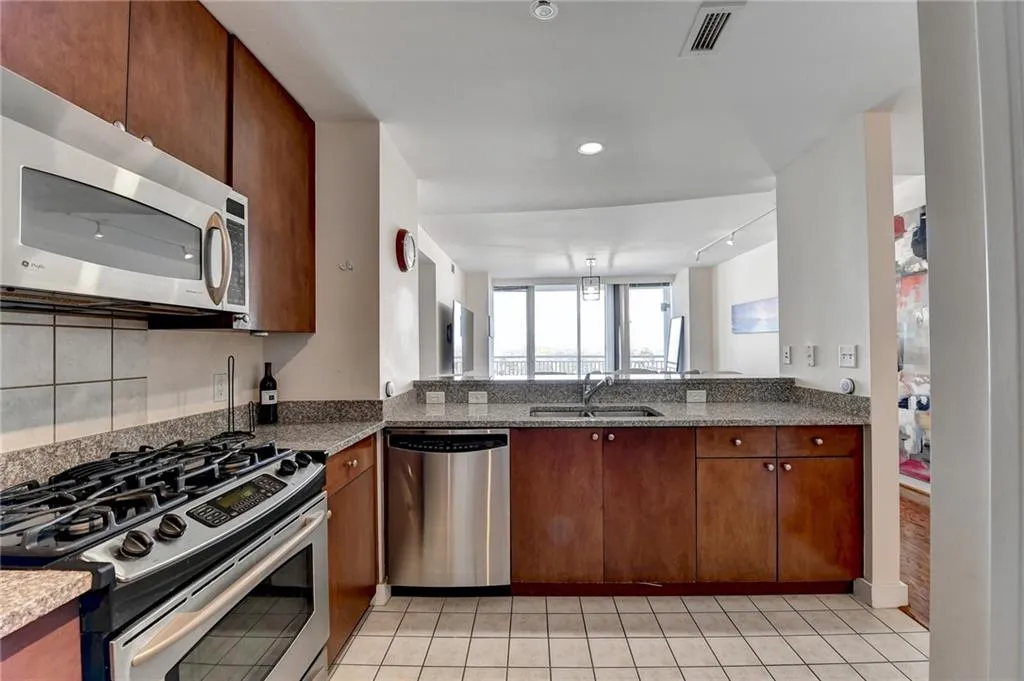 Kitchen featuring appliances with stainless steel finishes, stone countertops, light tile patterned floors, and sink